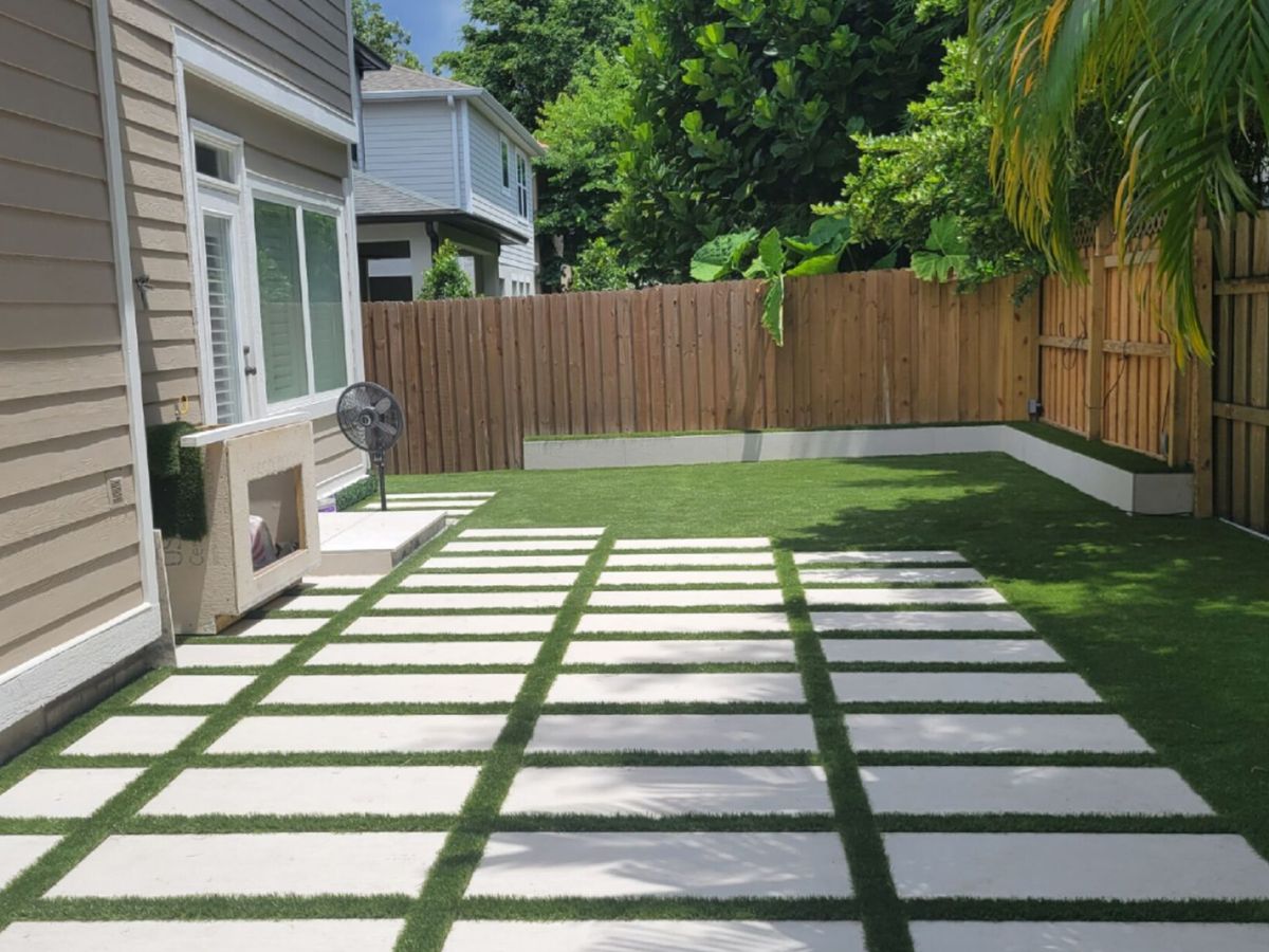 Backyard turf lawn with square pavers leading to a covered patio