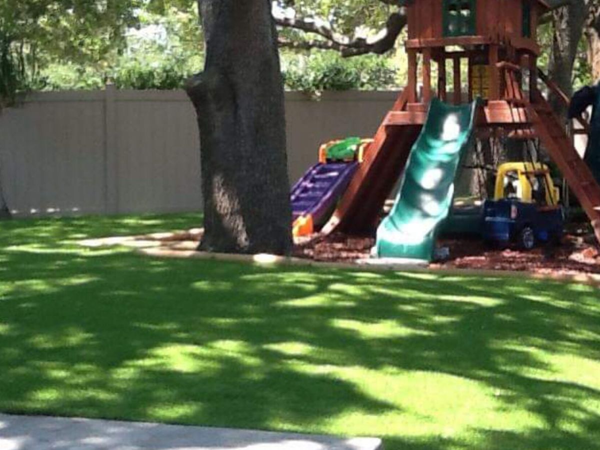 Backyard play set on new synthetic turf under a large oak